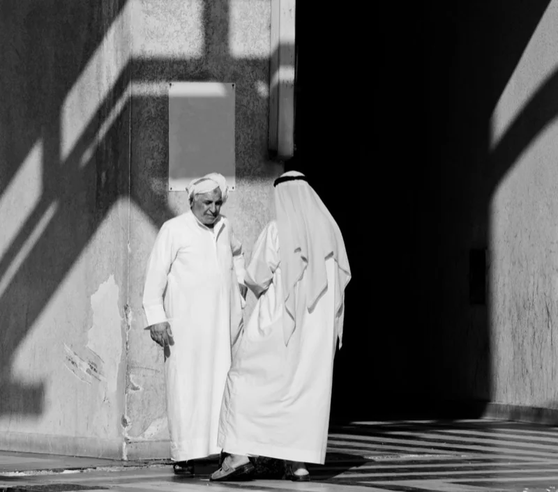 men in arab thawb robes talking on the sidewalk — illustrative editorial photography, not a verified location