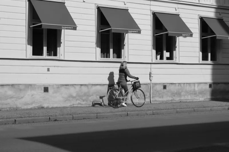woman walking with bike on sidewalk in town — illustrative editorial photography, not a verified location