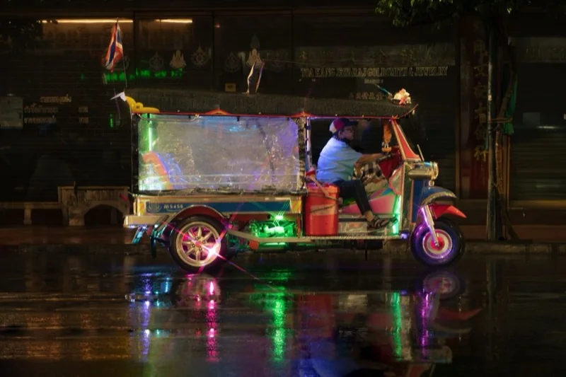 colorful tuk tuk at night on rainy bangkok street — illustrative editorial photography, not a verified location