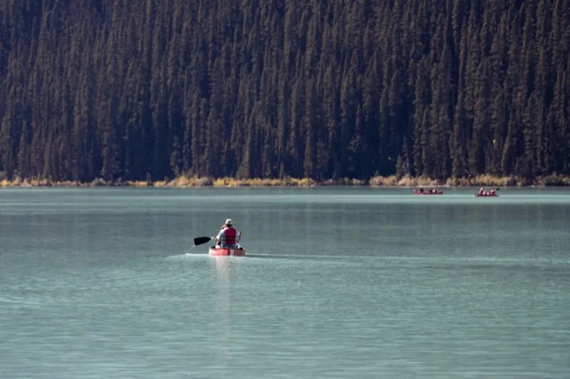 A paddler crossing a lake below a forested slope