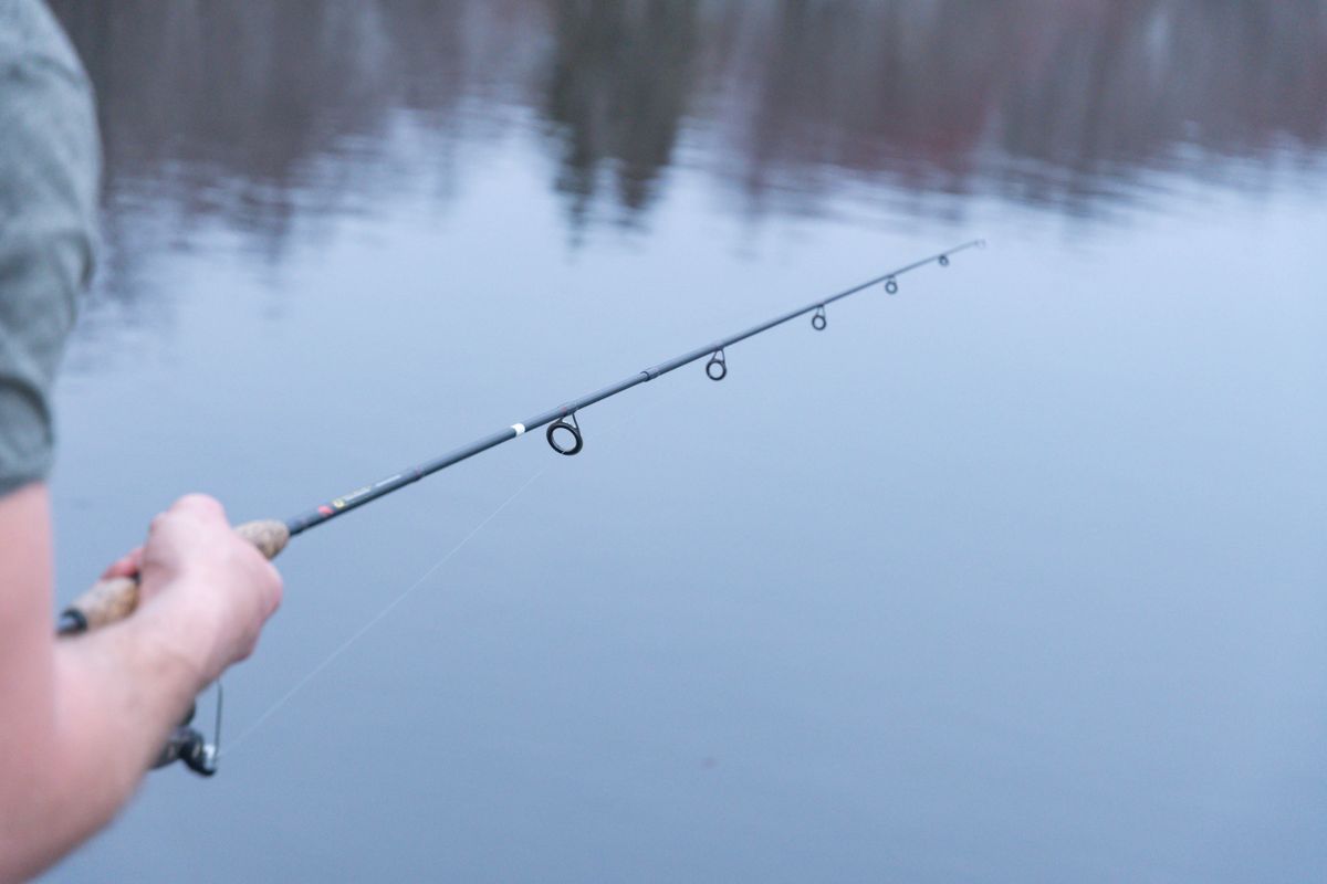 Hands holding a fishing rod above calm lake water